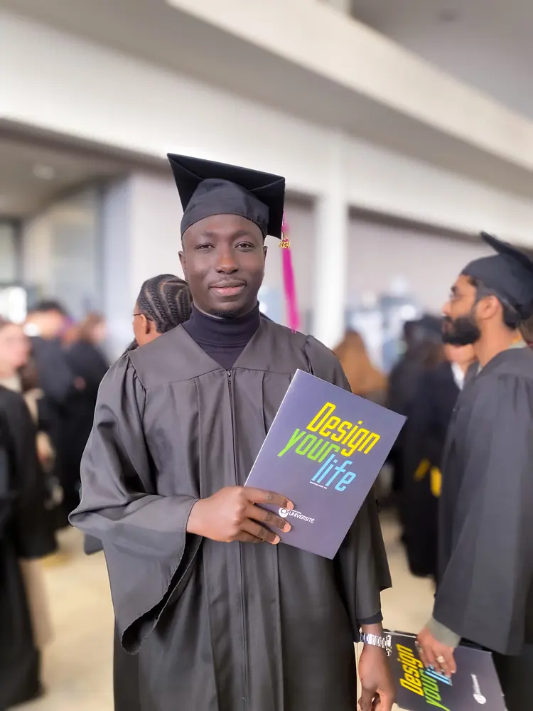Maname Wade en toge de diplômé, livret « Design your life » à la main