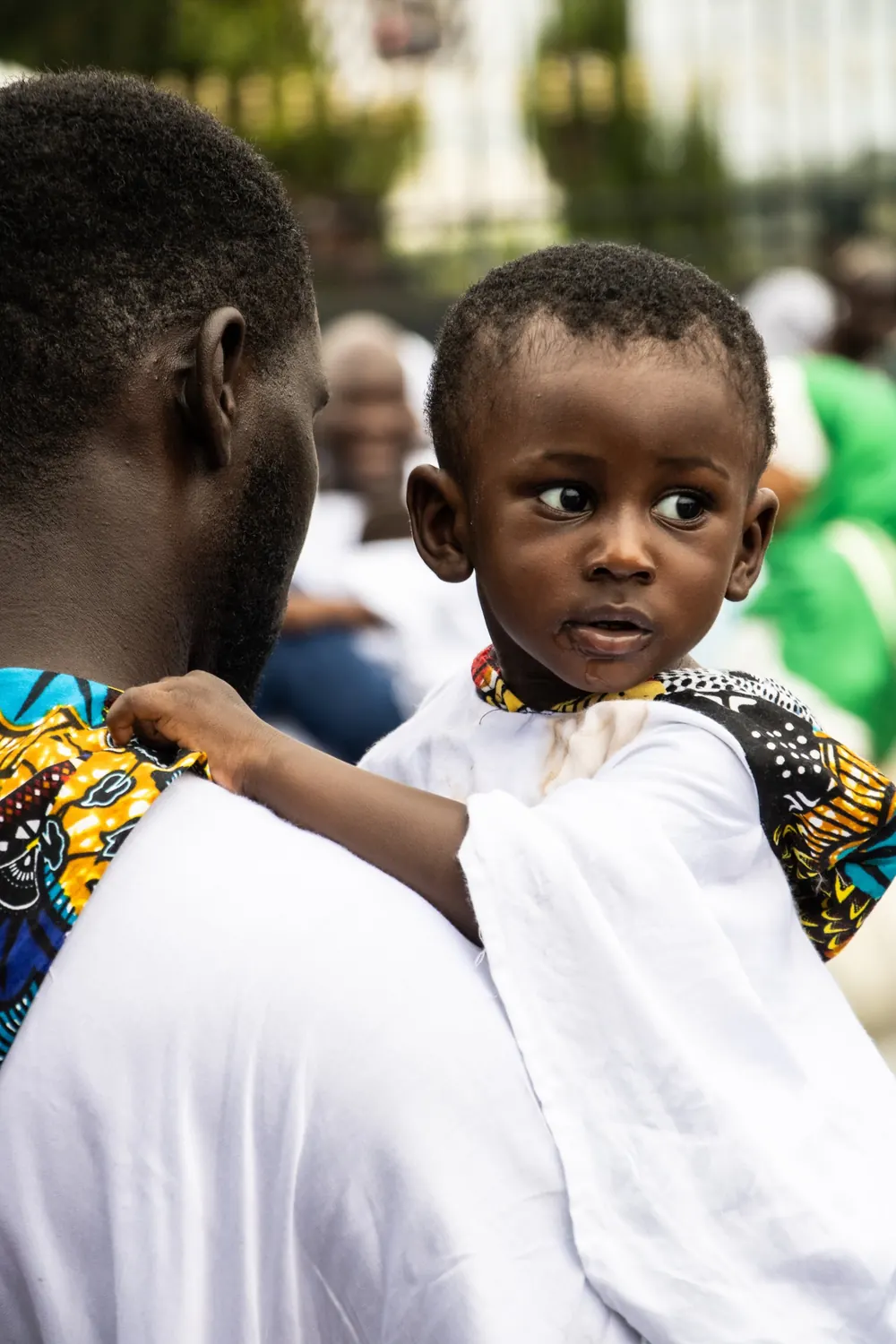 Un enfant dans les bras de son père regarde vers l’objectif